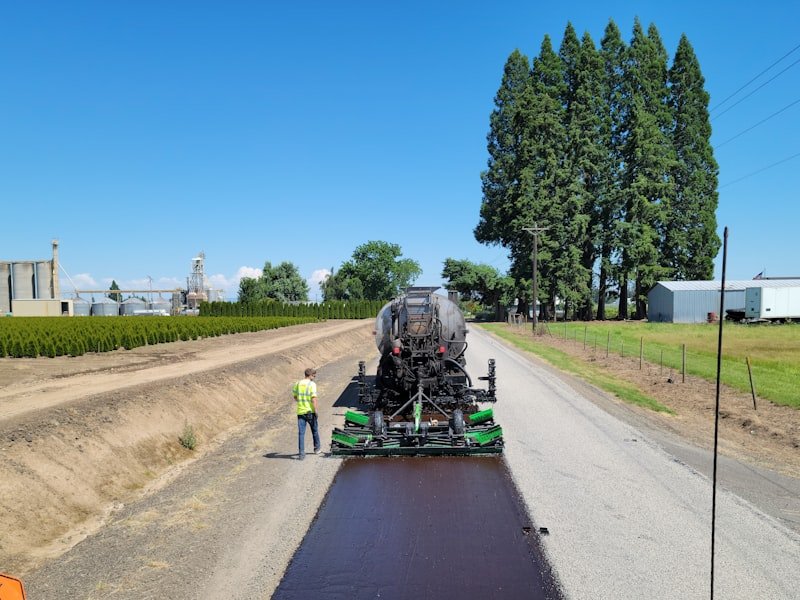 Operator running a paver as a fresh asphalt surface is laid